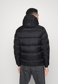 Svart puffjacka med huva, med en kviltad design och elastiska ärmslut. Slät textur, sitter tajt vid midjan och är lättviktig.