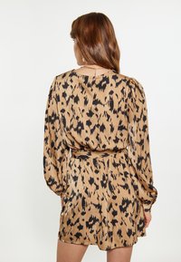Robe à imprimé animal en beige avec des taches noires ; présente des manches froncées et une ceinture à nouer à la taille. Tissu lisse et léger.