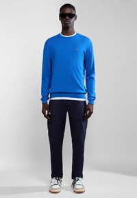 Maglione blu a maniche lunghe con scollatura a coste, abbinato a pantaloni cargo blu navy con tasche laterali e sneakers bianche con dettagli color tan.