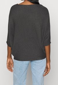 Dunkelgraues, locker sitzendes Strickoberteil mit weitem Ausschnitt und Dolmansleeves, kombiniert mit hellblauen Jeans. Texturiertes Material, lässiger Schnitt.