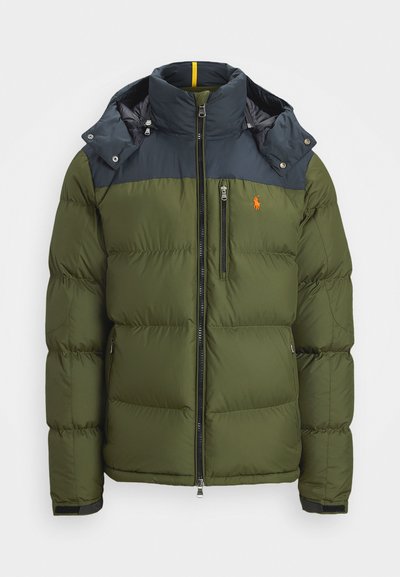 Olive green puffer jacket with navy shoulder panels, high collar, front zipper, chest pocket, and orange embroidered logo on chest.