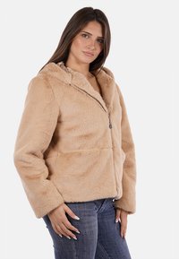 Giacca con cappuccio in pelliccia sintetica color beige chiaro, dotata di zip frontale, due tasche anteriori e una texture morbida. Progettata per calore e comfort.