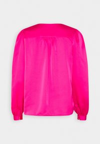 Blouse rose vif à manches longues avec empiècement froncé et poignets boutonnés, vue de dos sur un fond uni.