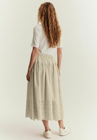 Ljusbeige knä-lång kjol med elastisk midja, med broderade detaljer och vågig fåll. Tillsammans med vita sneakers.