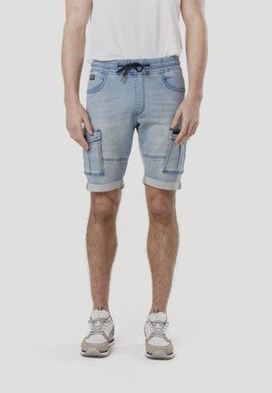 Világoskék farmerrövidnadrág gumis derékrésszel és húzózsinórral, két oldalzsebbel és feltekert szegéllyel. A szövet kopott textúrát mutat.