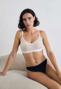 White bralette with a textured overlay, V-neck design, and thin straps, paired with black sheer panties. Light, breathable fabric.