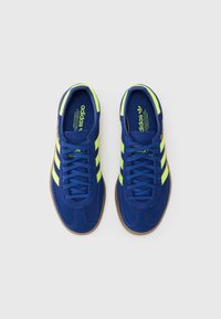 Blå ruskinds sneakers med neongule striber, flade snørebånd og en brun gummisål. Indersålen har branding i lyse farver.