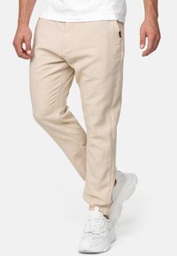 Pantaloni beige leggeri con vestibilità dritta, caratterizzati da tasche laterali e tessuto strutturato. Abbinati a sneakers bianche.