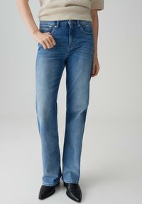 Jeans en denim bleu clair avec une coupe droite, taille mi-haute, et coutures visibles. Assortis à des chaussures noires à talons pointus.
