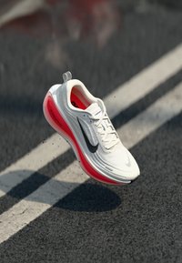 Chaussure de sport blanche avec un dessus texturé, logo Nike noir et amorti Zoom Air rouge sur la semelle, avec des lacets et une languette.