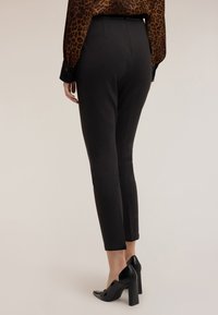 Czarne dopasowane spodnie o wąskim kroju, z wysokim stanem i gładką teksturą, zestawione z czarnymi szpilkami.