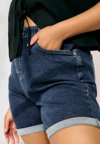 Jeansshorts i mörkblått med ljusblå rullade fållar, med en framficka och en slät yta, ihop med en svart topp.