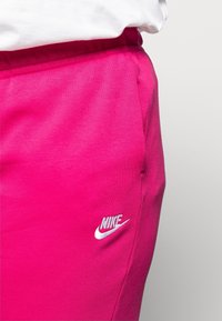 Fuchsiové Nike tepláky s elastickým páskem a bílým vyšitým logem na levém stehně. Měkký bavlněný materiál, minimalistický design.