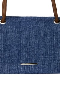Denim totetaske med brune læderhåndtag, med sølvhardwaredetaljer og en rektangulær metallisk akzent i midten.