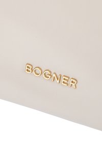 Beige tekstilpose med struktureret overflade og et fremtrædende gyldent "BOGNER" logo. Elegant, rektangulær form med minimalistisk design.