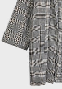 Tissu à carreaux gris et beige avec une manche droite et une poche fendue verticale sur un vêtement.