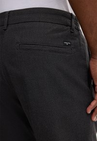 Charcoal textured trousers featuring a back pocket with a small logo tag. Waistband includes elastic for comfort and flexibility.