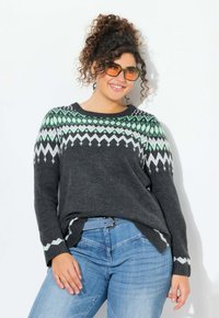 Maglione grigio lavorato a maglia con un motivo geometrico verde e bianco sul collo e maniche lunghe. Indossato con jeans azzurri chiari e una cintura abbinata.