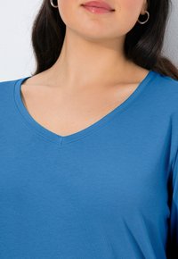 Niebieski t-shirt z dekoltem w serek i krótkimi rękawami, wykonany z miękkiej tkaniny. Gładka faktura z subtelnym przeszyciem przy linii szyi.