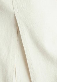 Tela de lona en blanco roto, con una costura visible y un detalle dividido, que muestra una textura suave y un color claro y uniforme.