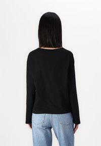 Svart langermet skjorte laget av mykt stoff med en avslappet passform. Kombinert med lyseblå høyt midje jeans, med baklommer og en falmet look.
