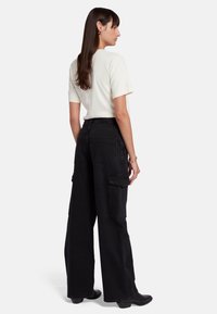 Pantaloni cargo neri a gamba larga con tasche laterali e posteriori, abbinati a una maglietta fitted color crema. Tessuto morbido, taglio moderno e dettagli minimal.