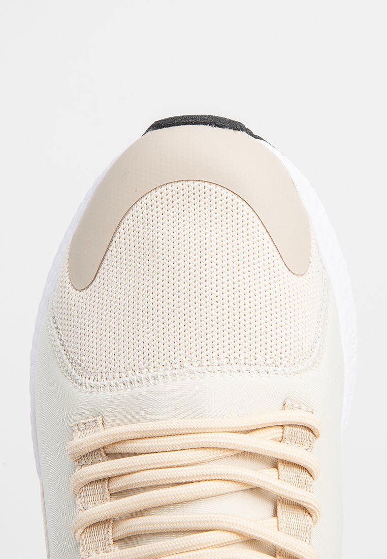 Kremowe sneakersy z siateczkową tkaniną na palcach, beżowym czubkiem i pasującymi sznurowadłami na białym tle.