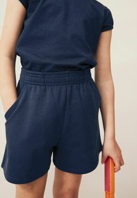 Shorts en coton bleu marine avec une large ceinture élastique, des poches latérales et une coupe décontractée, assortis à un haut à manches courtes.
