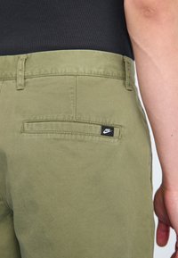 Ελαιόλαδο πράσινα παντελόνια από βαμβακερό μείγμα με πίσω τσέπη που φέρει ετικέτα μαύρου λογότυπου Nike, διακριτή υφή και κλασικό σχέδιο ίσιας γραμμής.