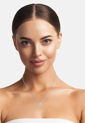 Collana d'argento con pendente floreale su una catena delicata, esposta su un modello con una carnagione liscia e uno sfondo neutro.