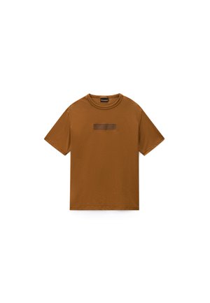 T-shirt marron en coton à manches courtes avec un col rond et un petit patch rectangulaire marron foncé centré sur la poitrine.