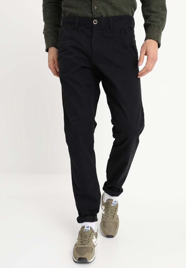 Svarta bomullbyxor med avslappnad passform, med bälteshällor, framfickor och knappstängning. Kombination med olivfärgade sneakers.
