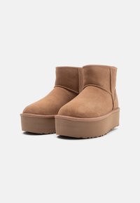 Botas de tobillo de ante marrón con punta redondeada, que cuentan con una suela de plataforma gruesa y una asa en la parte posterior. Detalles de costura a lo largo de las costuras.