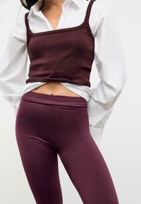 Top a canotta aderente bordeaux abbinato a leggings bordeaux a vita alta, realizzati in un materiale liscio e elasticizzato, con un design a tinta unita.