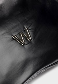 Czarny skórzany woreczek z wyraźnym metalicznym logo "W". Gładka tekstura z subtelnym połyskiem i delikatnie uformowanym kształtem.