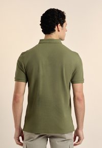 Polo de color verde oliva con tejido texturizado, mangas cortas y un cuello clásico. Presenta un corte relajado y aberturas laterales en el dobladillo.