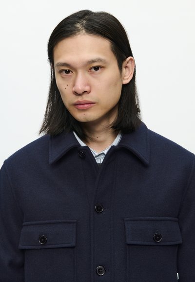 Dark navy wool jacket with two front pockets, button closure, and a fold-over collar. Textured fabric with a clean finish.