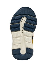 De zool van de schoen heeft een combinatie van blauwe rubber en witte textuursecties, met ventilatiegaten en graveringen van het merk. De patronen omvatten golvende lijnen.