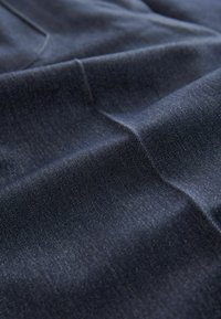 Tivă de denim de culoare albastru închis cu o textură netedă, având modele subtile de twill și o ușoară strălucire, expusă în pliuri și cute delicate.