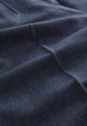 Mørkeblå denimstof med en glat tekstur, der har subtile twill-mønstre og en let glans, præsenteret i bløde folder og rynker.