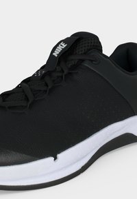 Μαύρο αθλητικό παπούτσι Nike με λευκή σόλα, πλέγμα άνω μέρος και μαύρες κορδόνια, εμφανίζεται από πλάγια γωνία σε λευκό φόντο.