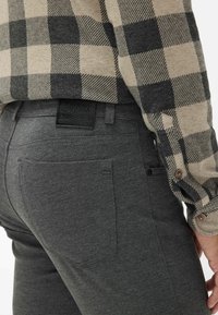 Pantaloni elasticizzati grigi con una vestibilità su misura, dotati di una patch con logo sulla cintura posteriore e due tasche posteriori. Il tessuto ha una consistenza morbida.