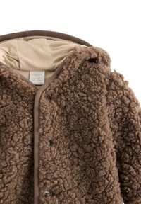 Brun fleecejakke med en tekstureret, fluffy overflade, beige foret og enkle knaplukninger. Har en rund krave og ingen synlige mønstre.