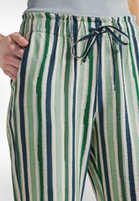 Randiga byxor i en blandning av mörkblå, grön och gräddfärg. Tillverkade av mjukt tyg, de har resår i midjan med dragsko.