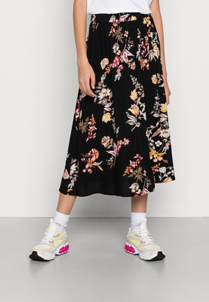 Zwarte midirok met kleurrijke bloemenprint, gecombineerd met witte sokken en witte sneakers met roze accenten, getoond van taille tot voeten.