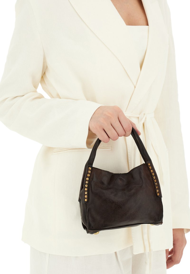 Borsa a tracolla in pelle nera con finitura texturizzata, manici corti e borchie dorate sui lati. Indossata con un blazer chiaro.