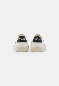 Weiße Sneaker mit schwarzen Akzenten, ausgestattet mit einem glatten Leder-Obermaterial, flachen Schnürsenkeln, einer strukturierten Sohle und markierten Fersenelementen mit dem "VEJA"-Logo.