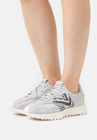 Zapatillas grises con un acento de patrón de cebra, hechas de ante y materiales sintéticos, con una suela de goma blanca y cordones texturizados.