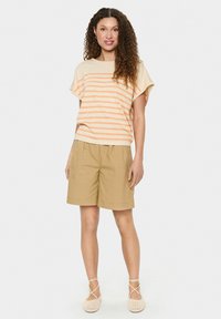 Gestreepte top met korte mouwen in crème met oranje strepen, gecombineerd met beige shorts. Model draagt beige geweven schoenen met banddetails.