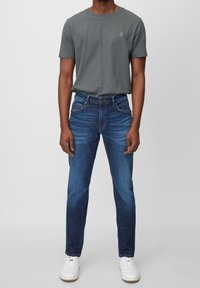 Camiseta de algodón gris de mangas cortas, combinada con jeans de mezclilla azul. Los jeans de corte slim tienen un desvanecimiento y costuras en contraste. Zapatillas blancas.